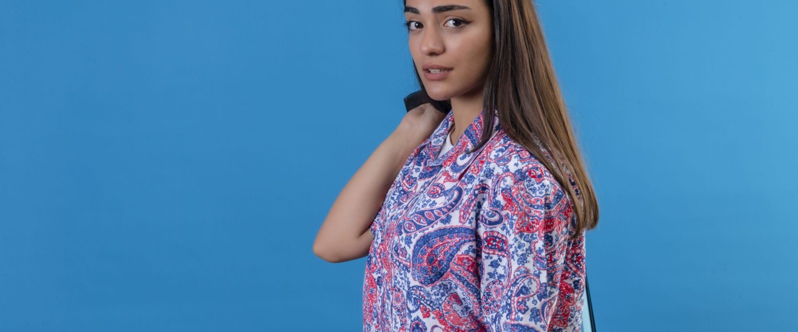 young beautiful traveler woman standing with blue suitcase looking uncertain and confused over isolated blue background